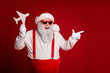 © deagreez - Cheerful Santa with red suspenders and hat holds plane cutout against red background for Christmas celebration festive marketing image