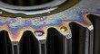 © Rikhy - Close-up of Gear with Iridescent Oil Spill, Engineering and Machinery Concept