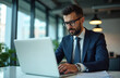 © Vadym - Man in suit and glasses types on laptop in modern office. Businessman works at desk by window. Focused person uses computer for job. Young executive checks emails indoors, remote work.