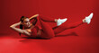 © Prostock-studio - A woman in bright red workout clothes is engaged in a fitness exercise. She is performing a core workout on a red background, showcasing strength and determination.