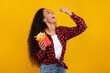 © Prostock-studio - A fit female model with curly hair happily eats French fries while posing against a vibrant yellow background. Her enthusiasm highlights a fun fast food moment and a love for snacks.