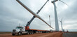 © Vadym - Crane lifts huge wind turbine blade from long truck at construction site. Heavy machinery assembles windmill for renewable power generation. Building green energy generator on wind farm, process of
