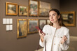© JackF - Woman in a jacket holds a mobile phone in an art gallery. European woman reads information about artists and a museum on her phone. Visitor to the exhibition uses an online guide