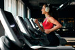 © Home-stock - Side view of young fit woman running on treadmill and listening to music via headphones during sports training in gym, copy space