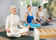 © JackF - Calm women of different ages meditating in Lotus Pose or Padmasana in beginning yoga training together in cozy gym studio