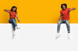 © Prostock-studio - Two people sit on a ledge with bright smiles, playfully pointing at each other. They are dressed casually, with one wearing a red shirt and the other in a similar style.
