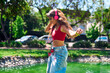 © Nano - Beautiful Latina woman dancing and listening to music, laughing and very happy in an outdoor park, wearing jeans and a red T-shirt, and pink headphones. Beauty, attitude, freedom.