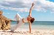 © Andrii - Woman in white activewear balances in Side Plank yoga pose on sunlit beach, reaching top arm toward sky. She enjoys outdoor exercise, combining strength and stability by the sea.