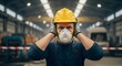 © SITI - Industrial Worker with Respirator and Hard Hat Covering Ears Due to Loud Factory Noise