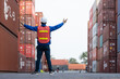 © eakgrungenerd - Back view of logistics worker in safety gear raising arms at container yard, symbolizing success, achievement, teamwork, cargo coordination in the global shipping industry.