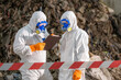 © BESTIMAGE - Two scientists in protective suits and masks analyzing documents outdoors in hazardous environment with warning tape and rocky background for safety research or environmental study