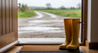 © val_webart - Yellow rubber boots placed at doorway on rainy day landscape