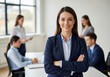 © smth.design - Confident businesswoman in formal attire smiling with arms crossed in modern office environment with diverse professional team