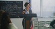 © Framestock - Female American Teacher Stands at Podium, Guiding Lesson With Humor and Warmth. Concept Modern American Teaching Methods, Classroom Communication, Student Centered Approach, Education Excellence.