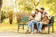 © Pixel-Shot - Happy family with warm plaid reading book on bench in autumn park