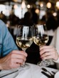 © SerPak - A couple clinks glasses of white wine in a cozy restaurant, celebrating a special moment together. The atmosphere is warm and inviting.