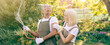 © Prostock-studio - A cheerful couple shares a light moment while watering plants in their garden. Bright sunlight filters through green leaves, highlighting their playful interaction and love for gardening.