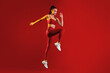 © Prostock-studio - A fit woman is captured mid-jump in striking red activewear on a vivid red background, showcasing her dynamic movement and athleticism. The scene conveys energy and determination.