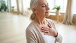 © David Zarzosa - Senior woman practicing mindfulness and relaxation breathing deeply with closed eyes and hand on chest at home.