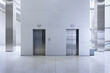 © mikelaptev - Clean, minimalist public interior features two stainless steel elevator entrances set in a light grey wall.