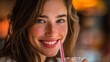 © maxximmm - A young woman with long hair is smiling warmly while holding a drink with a straw. The young woman’s joyful expression enhances the vibrant atmosphere of the setting.