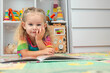 © Anna - Toddler girl in bright clothes playing and learning with a book on a colorful floor mat at home.