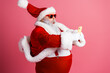 © deagreez - Santa takes a selfie in a red suit with white fur and sunglass using a smartphone against a pink background for Christmas season and festive mood