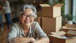 © Maryna - Happy senior Asian woman smiles while unpacking boxes during relocation. Elderly female enjoys new home living smiling at camera. Moving house transition is fun.
