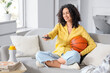 © Pixel-Shot - Female African-American sports fan watching basketball on sofa at home