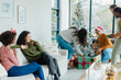 © Wavebreak Media - Diverse friends placing wrapped gifts under flocked Christmas tree holding cookie tray at home