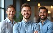 © Riley - A cheerful trio of businessmen poses for an office portrait. The young leader, executive director, and two team members of different generations smile at the camera. High quality