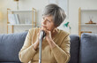 © Studio Romantic - Portrait of pensive elderly woman sitting on sofa at home, resting her chin on hands over cane. Thoughtful senior lady with gray hair looking away, reflecting on life moments or waiting for something.