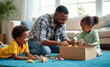 © Pete - African dad with two small kids putting toys into cardboard box. Fatherhood concept. Family cleans up mess. Dad and kids playing together at home. Father helps daughter and son clean room.