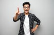 © Pete - Asian man points finger forward looking at camera with open mouth showing surprise. Guy wears glasses checkered shirt white t-shirt isolated on gray background.