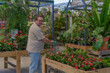 © Gesfera Images - Adult man selecting green plants and colorful flowers while pushing a shopping cart through a large greenhouse store