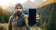 © Artfinity - Man hiking in a mountain landscape holding a black smartphone. Travel and adventure technology concept. Bearded hiker showing a blank mobile phone screen with a scenic backdrop.