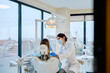 © we.bond.creations - Dentistry professional in a mask and gloves preparing to examine a female patient in a modern dental office