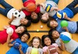 © Ozz - Diverse group of children smiling and holding sports balls on a gym floor