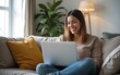 © wang - A woman is sitting on a couch and looking at a laptop. She is smiling and she is enjoying herself. High quality