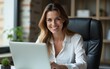 © nian - Attractive middle-aged businesswoman work seated on desk with laptop smile staring at camera. Portrait of company boss, successful businesslady, career growth and business opportunities, tech concept