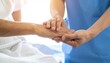 © gopin - Close up of Senior's Hand Being Held by Caregiver in Blue Uniform Offering Compassion and Support Against Soft White Background