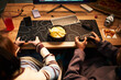 © DragonImages - Teenage Caucasian girl and Black teenage boy sitting at desk playing video games together using game controllers, sharing bowl of potato chips, computer monitor and keyboard visible
