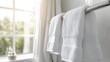 © Suphawan - Freshly laundered white towels hanging on a polished metal rack in a bright bathroom with natural light streaming through the window