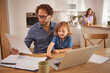 © Stockphotodirectors - A father reviews paperwork at the kitchen table while his daughter happily engages with him. Their mother prepares breakfast in the background, creating a warm family atmosphere.
