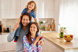 © Stockphotodirectors - A family enjoys time together in their kitchen. The child rides on dad's shoulders while mom smiles. The atmosphere is warm and joyful, filled with love and laughter.