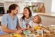 © Stockphotodirectors - A happy family shares breakfast in a bright kitchen. The parents playfully interact with their young child while enjoying a simple meal.