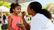 © Anna - Happy African American girl getting a butterfly face painting from an artist at an outdoor festival. Fun summer community event and childhood entertainment