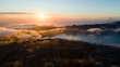© AmazingAerialAgency - Aerial view of the sun kissing the clouds over the rugged terrain, painting the sky with hues of orange and gold, Mount Batur, Bali, Indonesia.