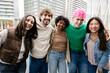 © Xavier Lorenzo - Five cheerful diverse students standing close together outdoors, posing for portrait while enjoying friendship and free time in the city. Youth, community and lifestyle concept.
