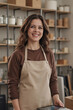 © AnnaStills - Portrait of Caucasian young adult woman smiling while standing in workspace holding digital tablet, shelves with jars and boxes in background, casual hairstyle, confident expression